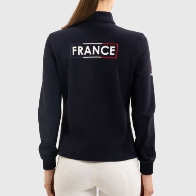 Femme en veste d'équitation Harcour Felicie noire avec casque et gants, menant un cheval. 2